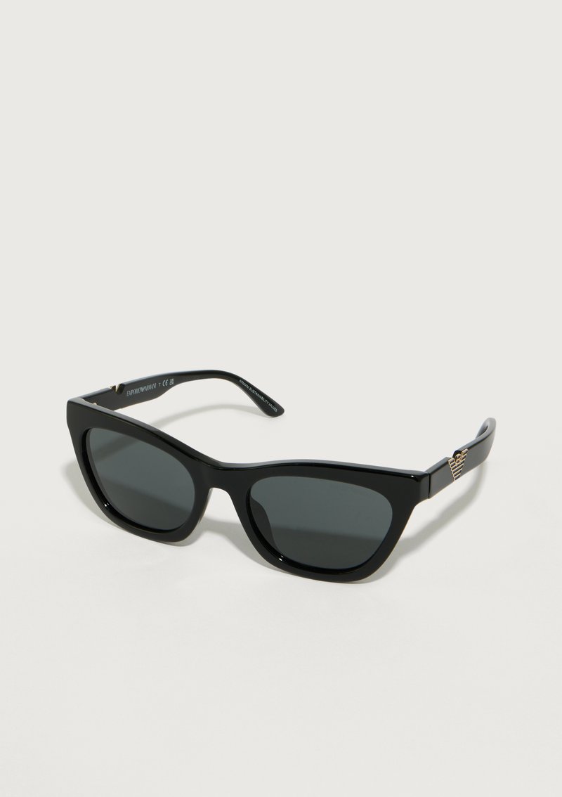 Gafas de sol cat-eye negras con lentes oscuras y detalle de logotipo dorado en las patillas, mostradas sobre un fondo claro.