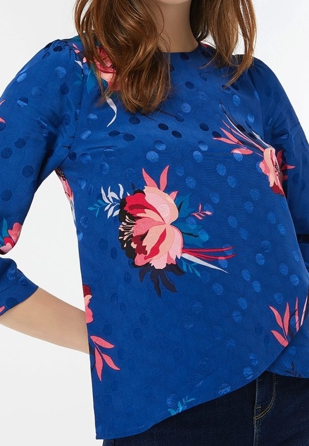 Blusa blu con motivo floreale in rosa e rosso, con pois, scollatura rotonda e maniche a tre quarti. Tessuto di alta qualità.