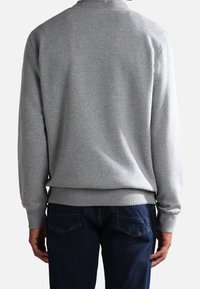 Felpa grigia con scollatura rotonda, polsini e orlo a coste, e texture liscia. Indossata con jeans blu scuro, che mostrano una vestibilità rilassata.