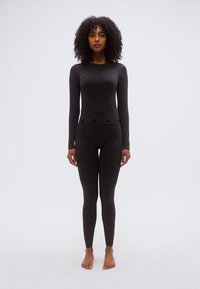 Μαύρο τοπ μακρυμάνικο και αντίστοιχο κολάν κατασκευασμένα από μαλακό, ελαστικό ύφασμα. Διαθέτουν υφασμένη ζώνη μέσης με διακριτικά μοτίβα.