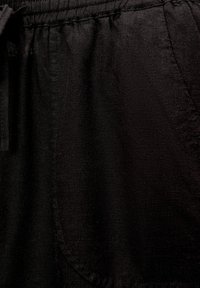 Pantaloni neri in lino con una texture morbida, vita elastica e tasche laterali. Il tessuto ha una finitura naturale e discreta.