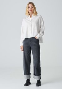 Weißes Hemd mit Knopfleiste und strukturierter Oberfläche, kombiniert mit dunkelgrauen weit geschnittenen Jeans mit hochgekrempelten Säumen. Schwarze ankle boots runden den Look ab.