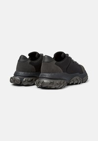 Black and gray athletic shoes featuring a thick, textured sole and sturdy canvas upper, viewed from the back.