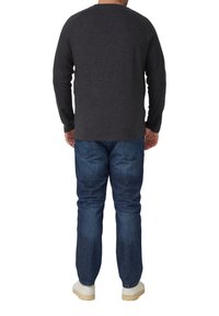 Dunkelgraues langärmeliges Shirt mit Raglanärmeln, kombiniert mit blauen Jeans und weißen Turnschuhen, von hinten gezeigt.