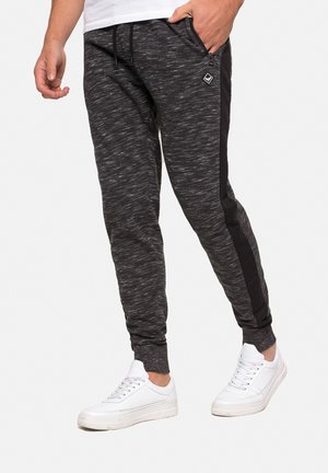 Grå melange joggerbukser med sorte sidepaneler, elastisk talje og ribkant, parret med hvide sneakers. Har en lynlåslomme.