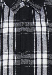 Randig skjorta i svart och vitt med knappar, med spridd krage, svarta knappar och en mjuk textur med ett rutmönster genom hela.