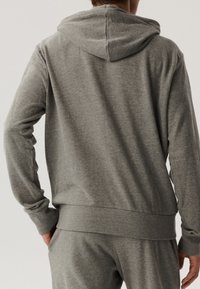 Szara bawełniana bluza z kapturem, długimi rękawami i ściągaczem u dołu. Materiał wydaje się miękki i teksturowany, z prostym wzorem.