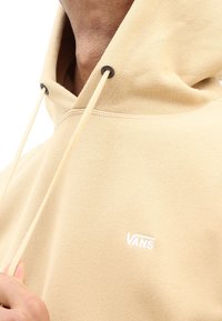 Hoodie in cotone beige con coulisse e un piccolo logo bianco. Presenta un tessuto testurizzato e una vestibilità casual e rilassata.