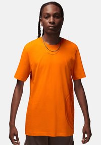 T-shirt a maniche corte in cotone arancione brillante con una vestibilità morbida, dotata di un collo rotondo e un discreto dettaglio del logo sulla parte anteriore.