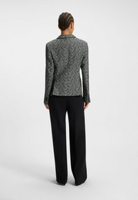 Skræddersyet blazer i sort og hvid houndstooth med lange ærmer, krave med hak og en struktureret pasform. Kombineret med brede sorte bukser.
