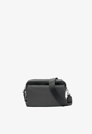 Kompaktowa czarna torba na ramię z regulowanym paskiem, przednią kieszenią, górnym zamkiem błyskawicznym i srebrnymi elementami na białym tle.