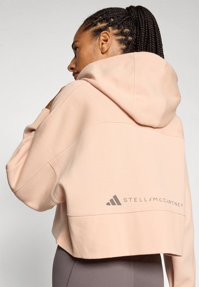 Skraćena, pastelno ružičasta dukserica od mekog materijala, s velikom kapuljačom i sivi logo "STELLA McCARTNEY" na leđima.