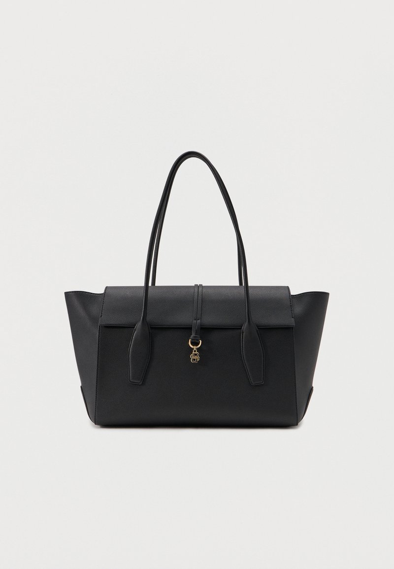 Sac cabas en cuir noir avec côtés structurés, double poignée, fermeture à rabat, et petit charm doré suspendu au centre avant.