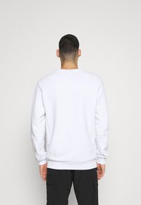 Bílá mikina s dlouhými rukávy, kulatým výstřihem, žebrovanými manžetami a lemem, s hladkou texturou a minimalistickým designem.