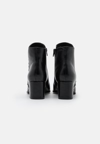 Botines de cuero negro con textura suave, tacón bloque de altura media y detalle de cremallera en la parte trasera. Diseño limpio sin patrones visibles.