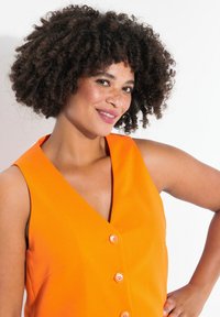 Felgekleurde oranje mouwloze jurk met een V-halslijn, vijf knopen langs de voorkant en een gladde stoftextuur.