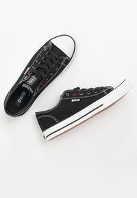 Sneaker in tela nera con punta e suola in gomma bianca. Presenta cuciture bianche, lacci neri e un piccolo logo sul lato.