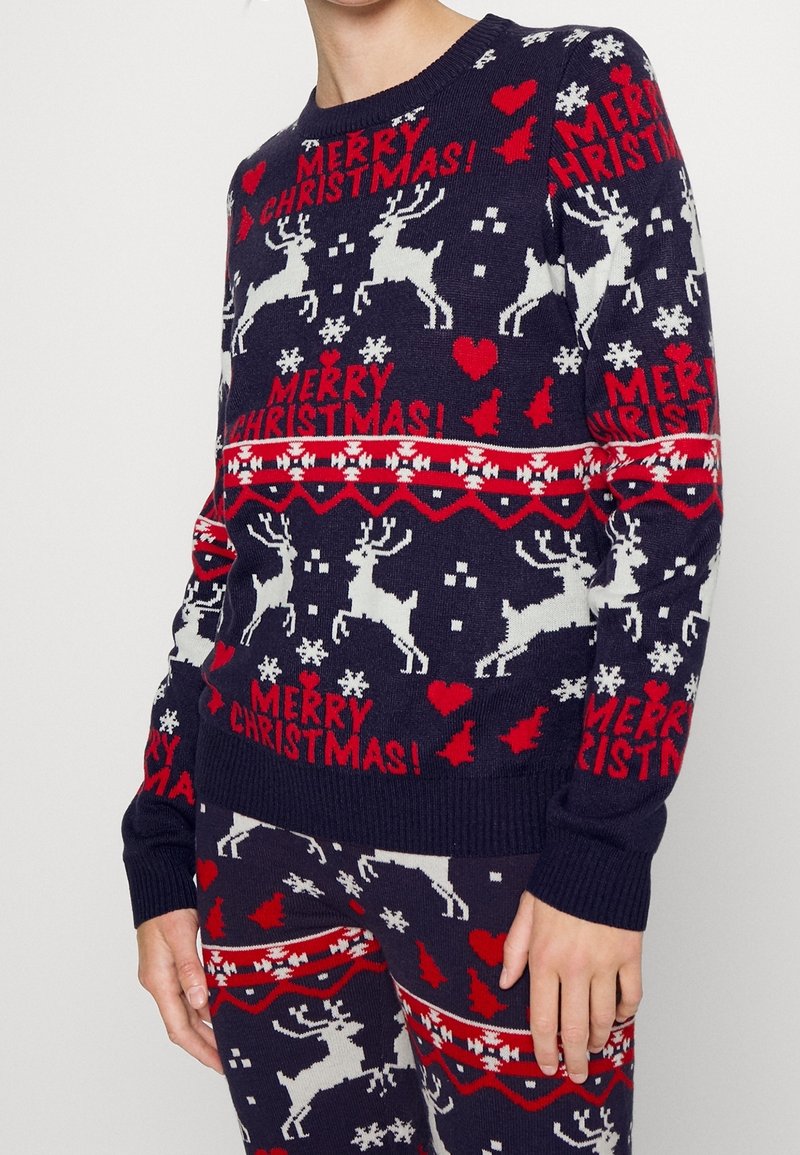 Marinblå jultröja med vita renar, röda hjärtan och snöflingor; ribbade ärmslut och nederkant; texten "GOD JUL!" i rött.