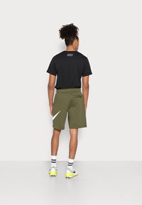 Schwarzes Kurzarmhemd mit grauem Nike-Logo auf dem Rücken, kombiniert mit olivgrünen Shorts mit weißem Nike-Swoosh-Detail.