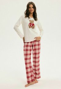 Biała piżama z długim rękawem z grafiką misia; czerwone spodnie do piżamy w kratę. Materiał wydaje się miękki i wygodny.