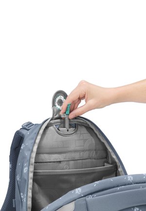 Hand pulling gray security lock tab inside open blue backpack with floral pattern and gray interior pockets.