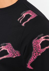 Camisa negra de manga larga con gráficos de jirafas rosas en los hombros. Tejido suave con una textura lisa, escote redondeado y diseño ajustado.