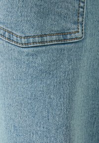 Světlomodrá džínovina s texturovaným povrchem. Obsahuje zadní kapsu se zlatým šitím podél okrajů.