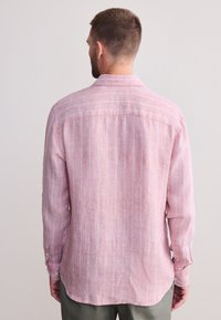 Ljusrosa långärmad skjorta med vertikala vita ränder, tillverkad av ett texturerat tyg, med krage som kan knäppas och rundad nederkant.