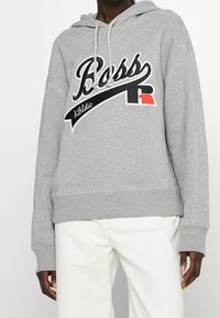 Grey hooded sweatshirt with a black and white "Boss" logo, athletic script, and red accent. Features ribbed cuffs and hem.