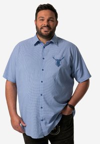 Camisa de manga corta, de botones, en un patrón de cuadros azul claro, con un emblema de un ciervo azul en el pecho y dobladillo redondeado.