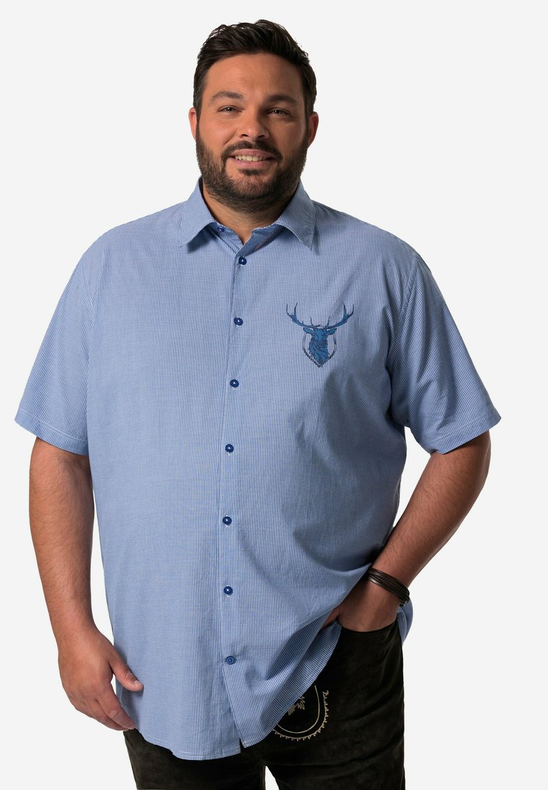 Camisa de manga corta, de botones, en un patrón de cuadros azul claro, con un emblema de un ciervo azul en el pecho y dobladillo redondeado.