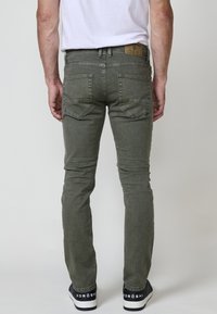 Olivno zeleni skinny jeans z teksturirano površino, pet žepov in blagovno znamko usnjenega obliža. Obuti z črnimi supergami s belimi detajli.