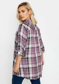 Camicia a maniche lunghe a quadri in viola, nero e bianco. Tessuto leggero con maniche arrotolate e vestibilità comoda. Presenta un dettaglio sul dietro.