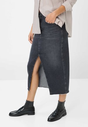 Dunkelblaue Denim-Midirock mit vorderem Schlitz. Getragen mit einer gestreiften Bluse und schwarzen Loafers, die mit strukturierten, glitzernden Socken kombiniert sind.