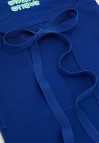 Blue cotton apron with a central bow, featuring a smooth texture and contrasting embroidered text in a lighter shade.