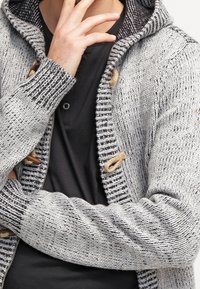 Grå stickad cardigan med en texturerad yta, med huva, träknäppningar och ett randigt foder inuti kragen.