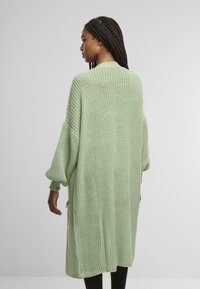 Lång, överdimensionerad cardigan i ljusgrön trikå. Har ribbade ärmslut, sidofickor och ett strukturerat mönster. Designen är avslappnad passform.