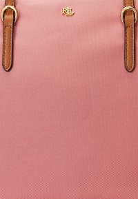 Różowa torebka z tkaniny o teksturowanej powierzchni, z brązowymi skórzanymi paskami i złotymi akcentami. Posiada logo "RIL" umieszczone w górnej części na środku.