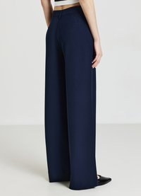 Marineblauwe weite Hosen mit glatter Textur, ausgestattet mit Gesäßtaschen und klassischem Schnitt, kombiniert mit schwarzen spitzen Ballerinas.