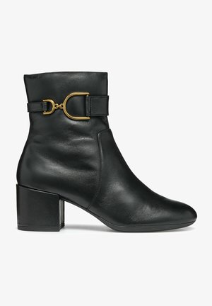 Stivale alla caviglia in pelle nera con punta tonda, tacco a blocco e dettaglio decorativo di una cintura con fibbia dorata attorno alla caviglia.