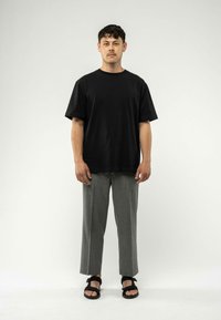 Zwarte katoenen t-shirt, losse fit, gecombineerd met grijze op maat gemaakte broeken en zwarte sandalen. Eenvoudig ontwerp, zonder patronen of opvallende details.