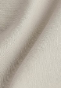 Tejido de algodón beige con una superficie suave y ligeramente texturizada, que presenta sutiles estrías diagonales y un caído suave.