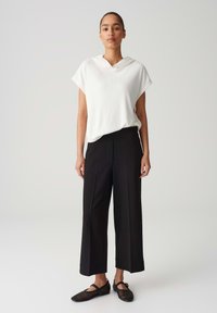 Top bianco a coste con maniche corte e cappuccio, abbinato a pantaloni neri a gamba larga e ballerine nere in rete. Design semplice e funzionale.