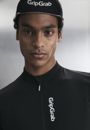 Fiatal férfi, fekete GripGrab kerékpáros sapkát és cipzáros kerékpáros mezt visel, melyen GripGrab logó van a mellkason és a sapkán.