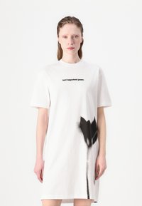 Balta medvilninė t-shirt suknelė, puošta juodu abstrakčiu gėlių raštu ir juodu užrašu „karl lagerfeld jeans“ ant krūtinės. Trumpi rankovės.