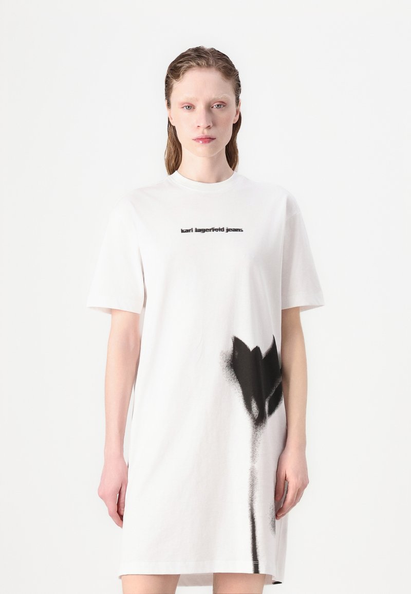 Balta medvilninė t-shirt suknelė, puošta juodu abstrakčiu gėlių raštu ir juodu užrašu „karl lagerfeld jeans“ ant krūtinės. Trumpi rankovės.