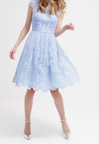 Ljust blått spetsklänning med en figurnära överdel, vågig fåll och korta ärmar. Har intrikata blommönster och en flödande kjol.