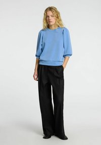 Gaiši zils, teksturēts džemperis ar puffed piedurknēm un apaļu izgriezumu, apvienots ar brīviem melniem biksēm un melnu apavu.