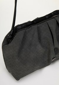 Bolso de tela gris texturizada con un diseño plisado, acentos de cuero negro y cierre con cremallera. Presenta una sola correa para el hombro.