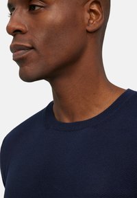 Marineblauwe gebreide trui met een ronde hals en een textuurpatroon, met close-up van het nek- en schoudergebied.